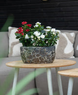 Eine künstliche Terrassenrose 35 cm creme UV steht auf einem runden Holztisch vor einem beigen Sofa mit gemusterten Kissen.