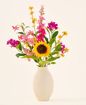 Der künstliche Blumenstrauß „Tiny Sunshine“ aus Seide befindet sich in einer beigen Keramikvase und besteht aus einem künstlichen Strauß lebensechter Blumen, wie einer großen Sonnenblume, rosa und magentafarbenen Blüten sowie gelben Blüten mit grünen Blättern, vor einem schlichten hellen Hintergrund. Dieses Arrangement von Easyplants besteht aus wunderschönen Seidenblumen, die jedem Raum langanhaltende Schönheit verleihen.