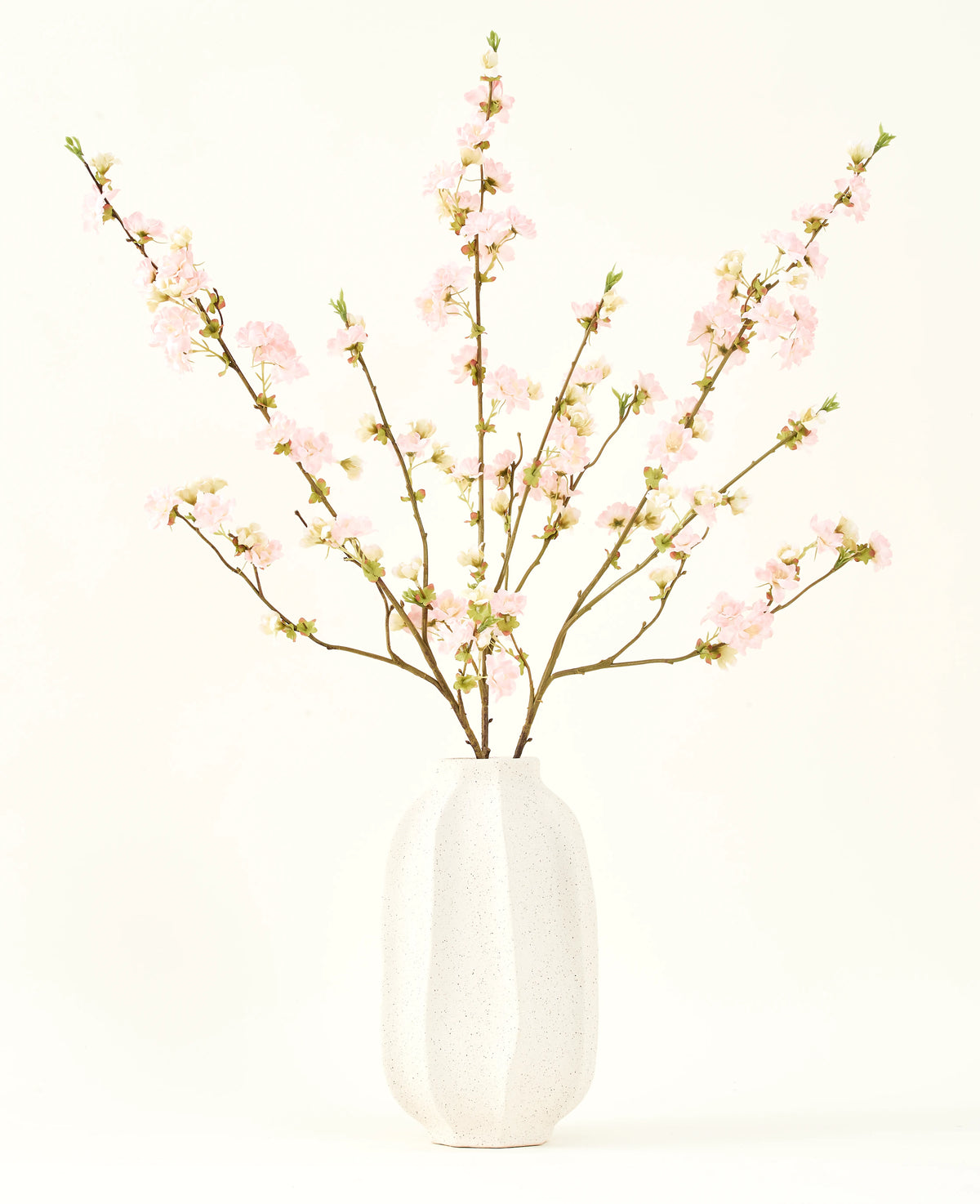 Der Seidenblumenstrauß Kirschblüten hellrosa 94 cm besteht aus zartrosa künstlichen Kirschblüten in einer weißen Keramikvase, die vor einem schlichten hellen Hintergrund Eleganz verleiht.