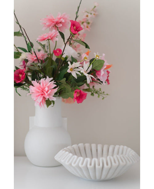 Eine weiße Vase mit einer künstlichen Blume Rhododendron Azalee 73 cm Fuchsia steht neben einer weißen Schale aus gerippter Keramik auf einer glatten Oberfläche vor einem neutralen Hintergrund.