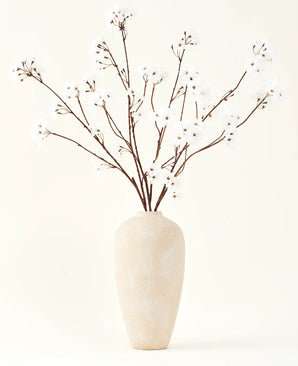 Der Seiden-Kunstblumenstrauß Kirschblütencreme 114 cm steht hoch in einer beigen Keramikvase und bringt mit seinen zarten, cremefarbenen Zweigen vor einem hellen Hintergrund eine heitere Dekoration in jeden Raum.