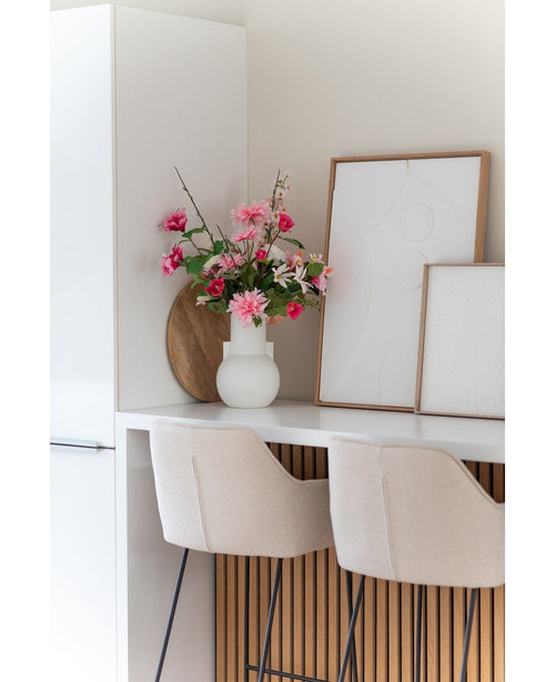 Eine moderne weiße Küche mit zwei beigen Barhockern, einer 68 cm großen künstlichen Dahlie in Rosa in einer weißen Vase auf der Theke und zwei gerahmten abstrakten Kunstwerken an der Wand.