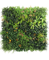 Die künstliche Hecke Marisa 100x100 cm UV ist eine üppige, quadratische grüne Wand mit gemischten Blattpflanzen, Farnen, gelbgrünen Akzenten und vereinzelten bräunlichen Blättern vor einem schlichten weißen Hintergrund.